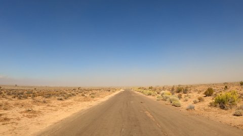 Driving down a desolate Mojave Desert road covered with sand by wind and storms - point of view