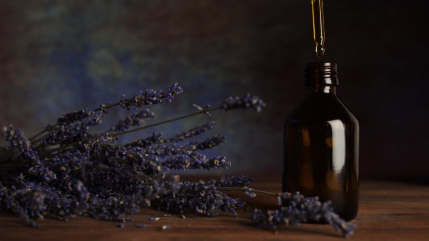 Natural lavender flower oil. Alternative medicine. Handmade cosmetics. A pipette with oil in hand, a dark glass bottle and lavender flowers on a wooden table.  | Shutterstock HD Video #1061844019
