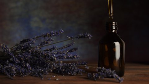 Natural lavender flower oil. Alternative medicine. Handmade cosmetics. A pipette with oil in hand, a dark glass bottle and lavender flowers on a wooden table. 