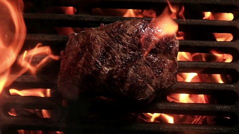Juicy steak tenderloin is fried on fire coals on iron grill on dark background. Barbecue in evening with friends at party. cooking dinner on open fire in hot bonfire flame. view from top