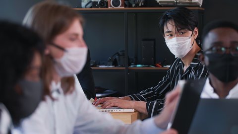 Racism at workplace. Young handsome serious Chinese businessman is stressed, left out at modern office wearing face mask