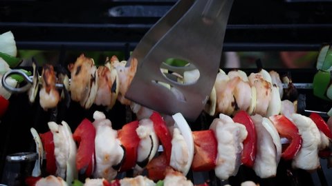 Turning Onion, Pepper and Prawn Barbecue Kebab with Metal Tongs