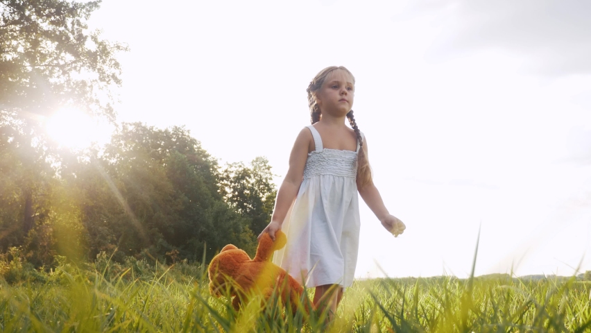 little girl kid walk with a teddy bear toy in the park in nature. childhood dream concept. smiling kid child walk with favorite toy lifestyle teddy bear dream of happiness in a green park outdoor