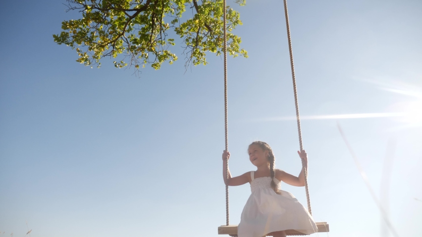 Little girl kid swinging on a wooden swing on a tree in the park. happy family kid dream concept. little kid girl playing on wooden swing on tree dream fun concept in park | Shutterstock HD Video #1061849722