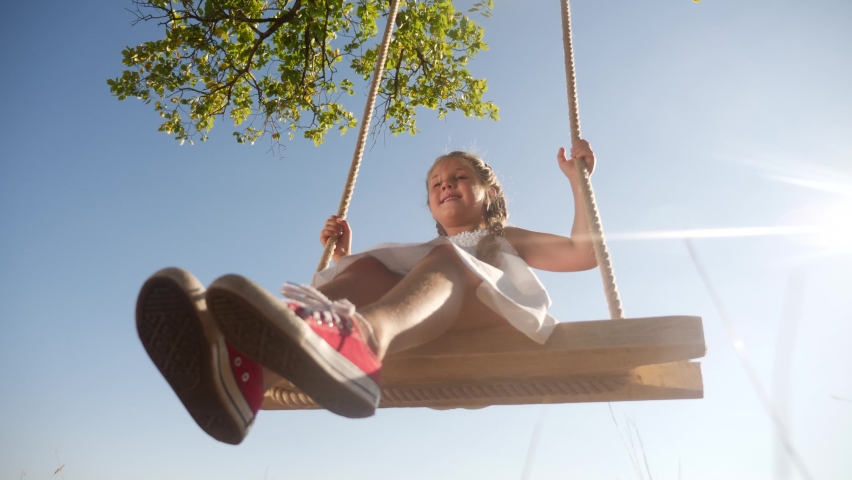 Little girl kid swinging on a wooden swing on a tree in the park. happy family kid dream concept. little kid girl playing on wooden swing on tree dream fun concept in park