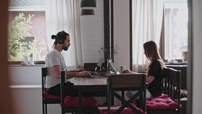 A young man and a young girl are working in front of laptops in their bright apartment. Work from home during quarantine. Remote work of freelancers.