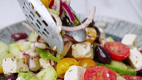 Arranging Greek Salad ingredients with a tong into a serving plate in 4K. Concept of a chef arranging a vegetable salad for being served.