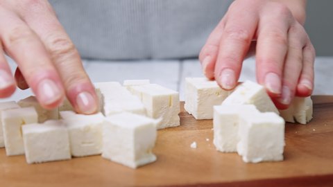 Close-up of Cutting/slicing cubes of feta cheese on a board for a Greek Salad.