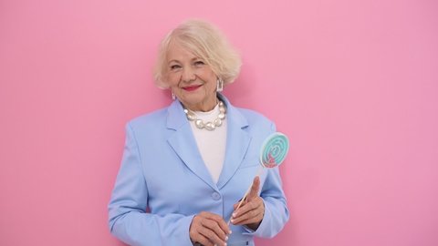 Happy Mature lady with blonde hair in a stylish blue suit posing holding a Lollipop, Studio shot.