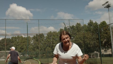 Happy retiree woman playing tennis and win. Sport and active lifestayle theme. Slow motion video.