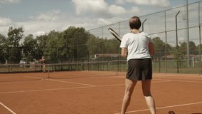 Slow motion video of senior women doing sport and playing tennis outdoor on tennis court to stay active and fit.