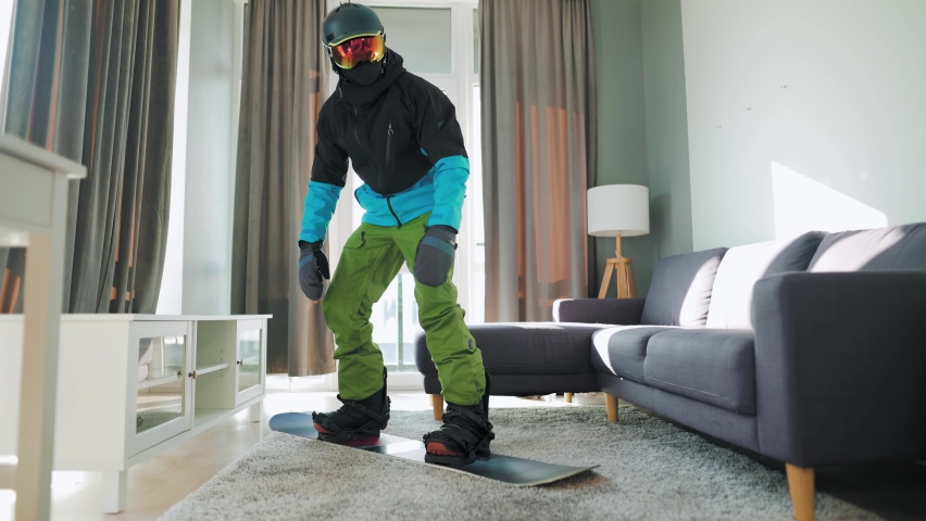 Fun video. Man dressed as a snowboarder rides a snowboard on a carpet in a cozy room. Waiting for a snowy winter Royalty-Free Stock Footage #1061855455