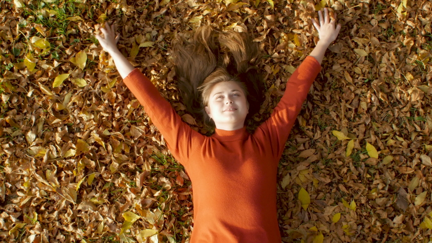 romantic beautiful young girl lying in autumn foliage and enjoying life. Pretty woman on dry leaves background in park top view