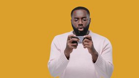 Excited guy playing games on mobile phone on yellow background