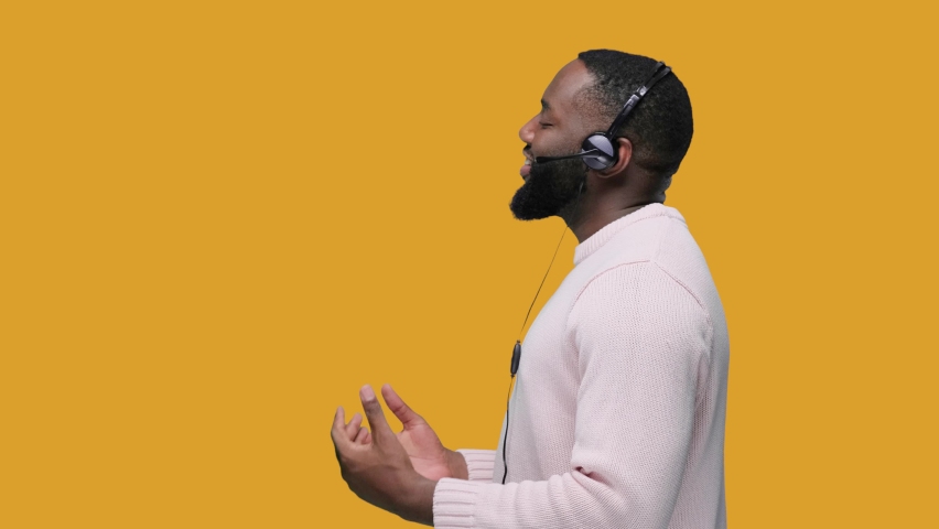 Smiling african american man wearing wireless headset talking to microphone, call center service. on yellow background Royalty-Free Stock Footage #1061858062