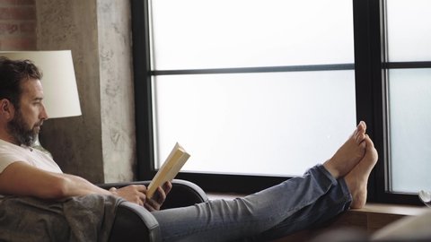 A relaxed man reading a book on the sofa at home 