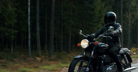 MED TO CU TRACKING Biker riding his custom built vintage retro motorcycle on a scenic forest road. Shot on RED cinema camera with 2x Anamorphic lens