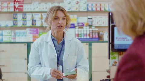 Young woman pharmacist serving a customer in a drugstore. Conversation pharmaceutical client. Seller commercial health care buyer uniform. Slow motion