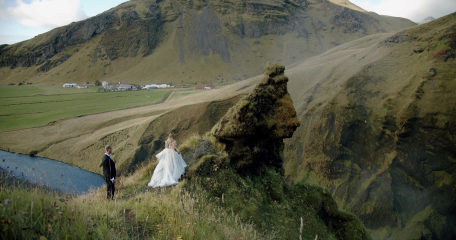 Wedding couple, the groom comes to the bride on the background of a waterfall. Iceland Wide shot