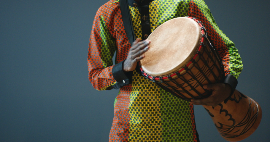 Close up of African American male hands tapping and drumming on bongo. Musician in traditional clothes. Tribe drummer from Africa playing on drum. Musical performance.