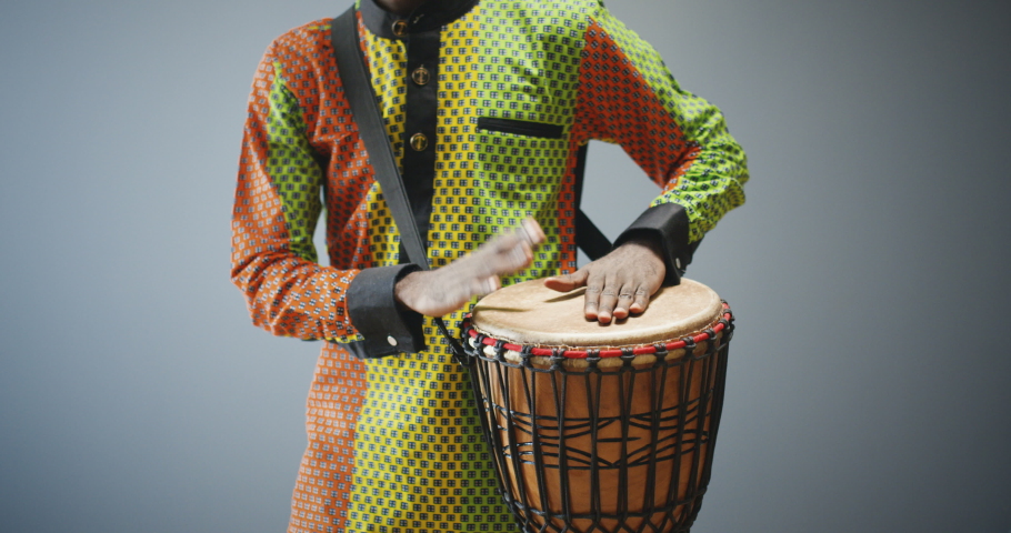 Portrait of male African American musician tapping on drum and smiling cheerfully to camera. Handsome man in traditional outfit playing on bongo with happy face. Musician with musical instrument.