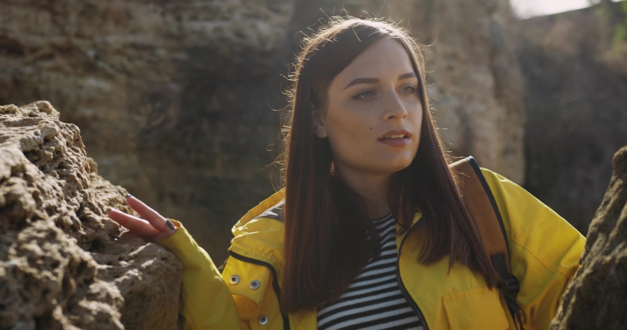 Close-up of beautiful girl tourist in yellow jacket walking among the rocks and stones, looking everything around.