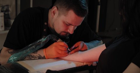 Portret tattoo artist draws a picture on the hand, the process of creating a tattoo. Slow motion.