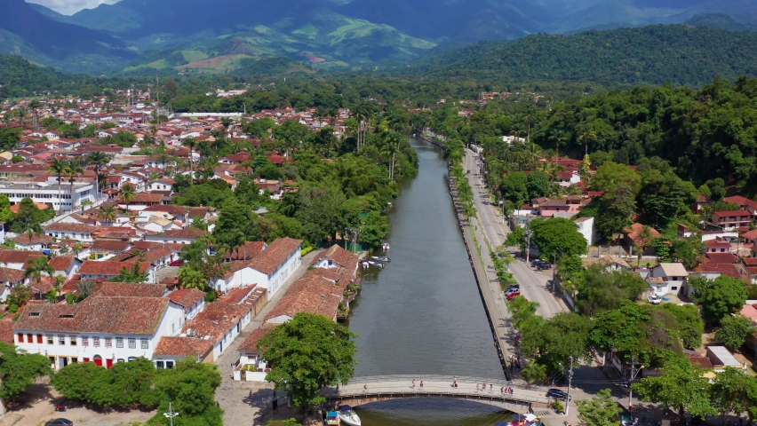 Aerial view over a river in the city of Paraty, towards mountains and the Serra da Bocaina National Park, sunny day, in Brazil, South America - tilt up, drone shot