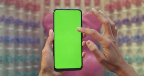 Close up view of female hand holding smartphone while scrolling and pressing on mockup blank screen. Concept of green screen and chroma key. Colourful background