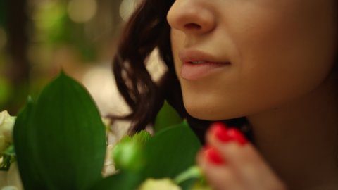 Happy woman smelling flowers in park. Closeup romantic girl holding rose bouquet outdoors. Portrait of gorgeous bride putting roses close to face in garden.