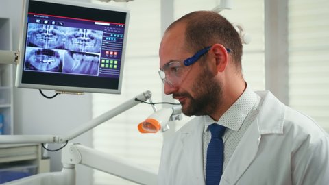 Portrait of stomatologist telling the treatment to elderly woman having digital x-ray in background. Doctor working in modern stomatological office explaining radiography of teeth from digital monitor