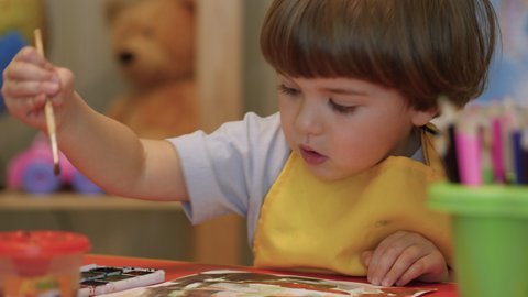 Four Year Old Caucasian Boy Having Fun Paints Picture On Paper, Being Creative and Artistic. Close Up Portrait Child Draws With Colored Paints on Paper. Cute Little Child Boy is Sitting and Painting.