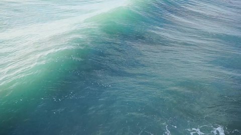 Overhead shot of huge rolling turquoise waves appearing on the sea, slow motion
