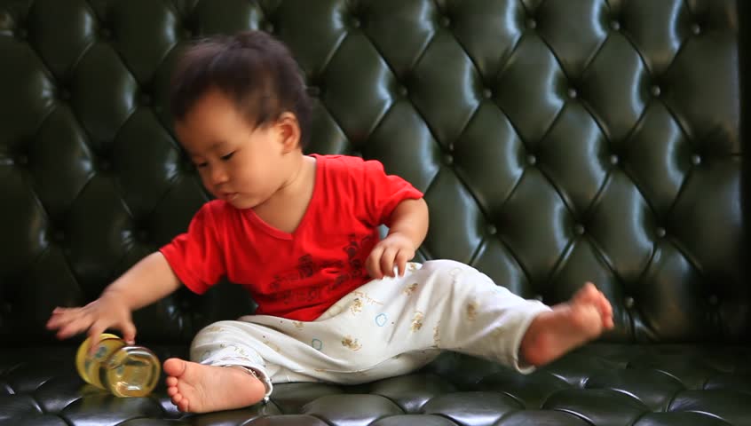 asian children playing with milk bottle on luxury leather sofa bed in home living room 