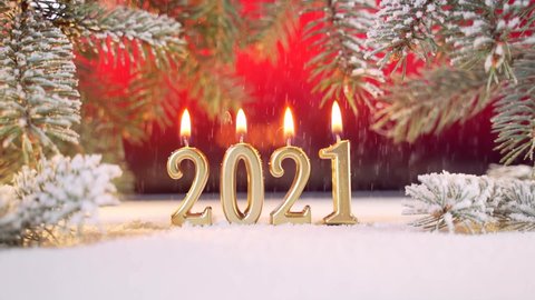 Close up. New Year's date golden candles are burning 2021. It's snowing. Snow falls. on the branches of a Christmas tree or pine a red background. Macro. Place to insert text. Copy space