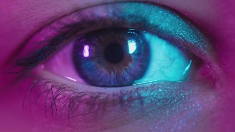 Close up shot of eye opening with blue iris. Healthy eyesight concept. Female blue eye in neon light. Young sexy girl in a nightclub. Macro look of the human eye. Pink-blue-green color, euphoria.