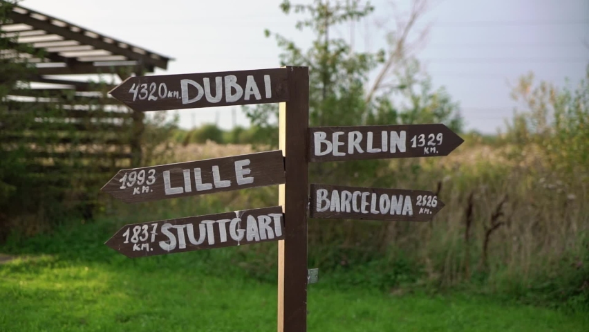 Old wooden road sign arrows with directions - Dubai, Berlin, Lille, Barcelona, Stuttgart at sunset