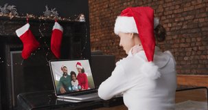 Caucasian woman spending time at home wearing santa hat, sitting by fireplace having video chat with friends on laptop screen, in slow motion. self isolation at christmas time during covid 19