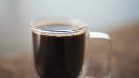 Smooth backward 4k view of a full glass coffee mug above a concrete surface with a gray and blurry background