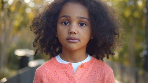 Close up portrait of serious little african girl looking at camera. Portrait of adorable preschool afro-american kid standing in ark over blurred background