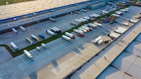 Logistics park with a warehouse - loading hub. Semi-trucks with cargo trailers standing at the ramps for loading/unloading goods at sunset. Aerial hyper lapse (motion time lapse).