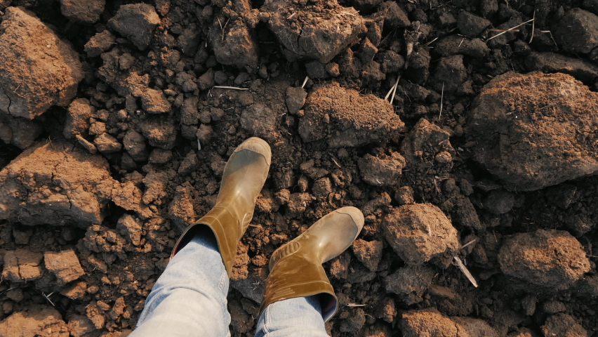 Top view closeup legs of a male farmer in rubber boots standing on a dry plowed field