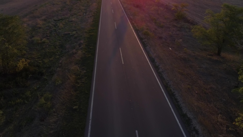 aerial shot, motorcyclist in safety helmet rides bike on road reflecting suns rays at sunset through fields after harvest Royalty-Free Stock Footage #1061903251