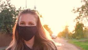 Front view, a young beautiful girl in a medical black mask on the background of a beautiful sunset looks at the camera. - Powered by Shutterstock - Get 15% off with code: PIKWIZARD15