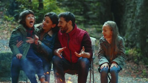 Happy family sits near campfire on autumn. Children with their parents are resting in the woods. Childhood relationship camping. Close up. Slow motion