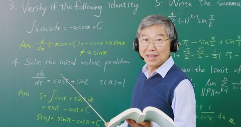 Asian senior male calculus professor wearing headset is teaching online with blackboard in classroom at university school