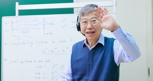 Asian mature male professor wearing headset is teaching Engineering online through webcam in classroom at graduate school