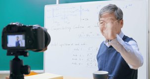 Asian mature male professor having online class is using digital video camera record during teaching math course at graduate school to prevent coronavirus infection