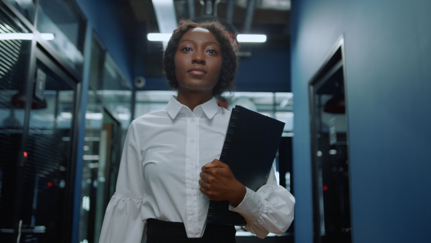 Portrait of focused businesswoman walking on meeting in office corridor. Closeup african american woman walking in corridor. Serious afro business woman going with folder in business center hallway. | Shutterstock HD Video #1061926930