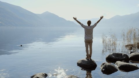 Young man standing arms wide open by the lake contemplating nature.